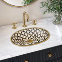 Oval bone inlay bathroom sink with geometric black and white pattern and brass rim, paired with gold faucet fixtures and cross handles on white marble countertop
