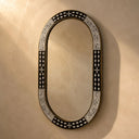Decorative oval mirror with intricate black and white frame on a beige wall.