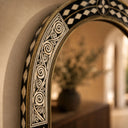 Decorative mirror with intricate black and white pattern on a wall.