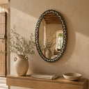 Decorative mirror with a vase and plant on a wooden console against a beige wall.