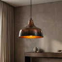 Hammered brass interior surface reflecting warm light from an Edison bulb inside a pendant lamp.