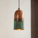 Handcrafted oxidized copper cylinder pendant light with hammered texture and green patina finish suspended from a black cord.