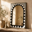 Decorative mirror with black and white geometric pattern on a wall with a plant and candle.