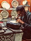 Man working on a piece of pottery in a workshop with various ceramic items in the background.