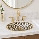 Bathroom vanity with gold faucet, geometric-patterned sink, and round mirror.