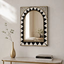 Decorative mirror with black and white geometric pattern on a wall above a table with books and a vase.